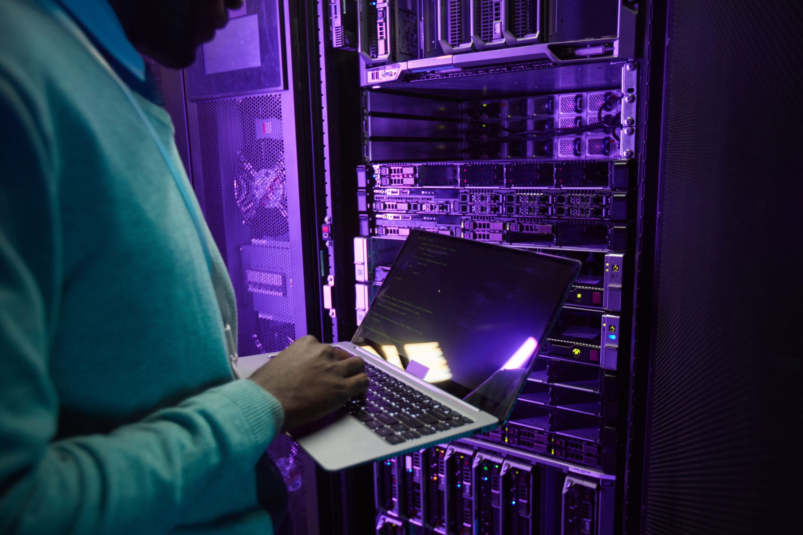 IT Engineer Using laptop in Data Center A person stands in a server room while using a laptop.