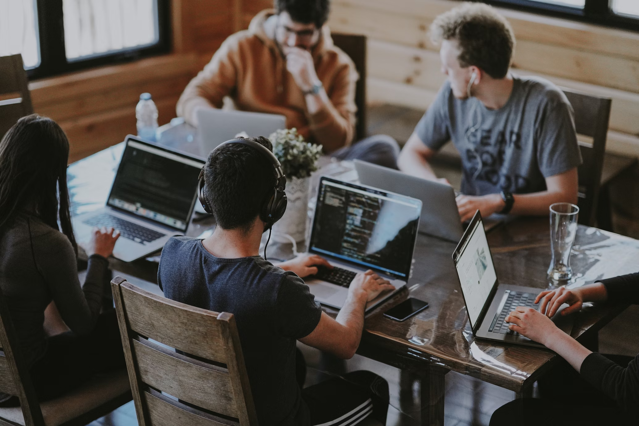 A group of people sit at a communal table and work on their laptops together. A group of people sit at a communal table and work on their laptops together.